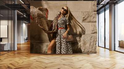 Elegant blonde model in fashionable leopard dress is sensually walking in the city on a summer day. Outdoor shoot. Wall mural