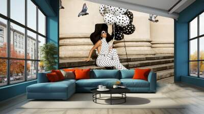 Spring, summer fashion. Glamour, stylish elegant woman in polka dot jumpsuit and big hat is holding balloons with dots. Fashion model in outfit with polka dots in the city. 60's style. Retro fashion Wall mural