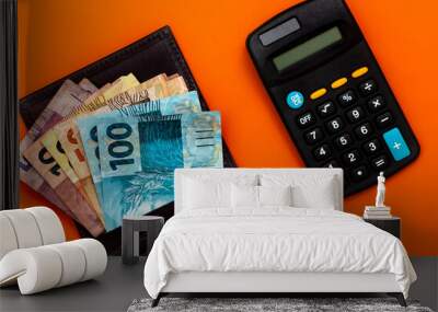 Brazilian money in wallet, with notepad, pen and calculator. Finance and salary concept. Economy of Brazil. Orange background Wall mural