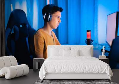 Focused gamer playing an intense online match at home. Surrounded by colorful tech gear, headphones, and neon lighting, perfect for streaming or esports tournaments Wall mural