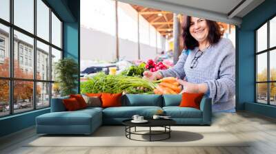 Mature woman smiling while picking carrots to buy at farmers market Wall mural