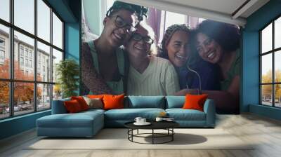 Adult daughters sitting around older mature mother on couch together. Generational South American women hugging mom indoors on sofa 2 Wall mural