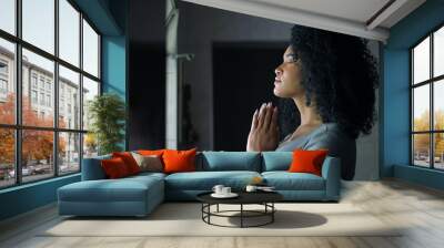 An African woman praying to God standing at home by window Wall mural