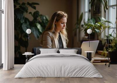 Working woman in a casual outfit, video conferencing on her laptop from her stylish, minimalist home office, wooden desk, Macbook Pro, notepad, natural sunlight, green indoor plants in the background Wall mural