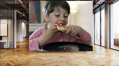 Child enjoying a slice of pizza at the dining table, capturing the joy and innocence of childhood during a meal. child's content expression and the act of eating Wall mural