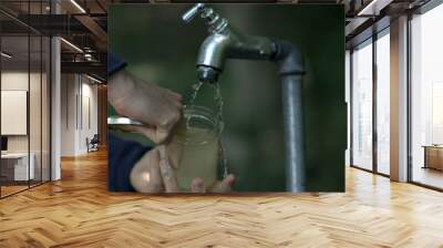 Cleaning a jar under an outdoor tap, slow-motion capture of water flow and hand interaction, emphasizing clean and refreshing hydration Wall mural