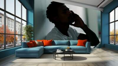 Concerned man sitting on floor at home feeling grief and regret. Silhouette of black man in the shadows Wall mural