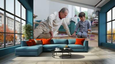 Elderly man and young boy playing card game on living room floor, boy enthusiastically placing cards while grandfather looks on, sharing intergenerational joy and family connection Wall mural