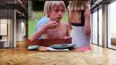 Handsome blond young boy eating cookie candid and real life family scene with children in background Wall mural