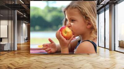 Little girl biting apple eating fruit outside Wall mural