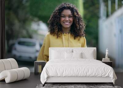 One happy confident young black woman walking in street looking at camera smiling. Portrait of a joyful African American girl in 20s with yellow blouse Wall mural