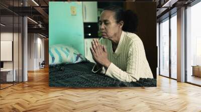 One senior hispanic woman praying to God by bedside. A spiritual older latin black person Wall mural