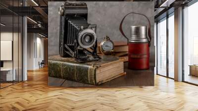 Antique bellows camera on an antique book with a thermos of coffee and a pocket watch next to it Wall mural