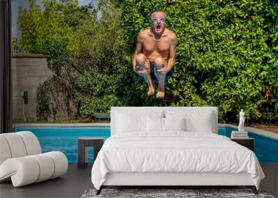 Middle-aged white man with a funny expression dives into the pool with swimming goggles, cannonball style Wall mural