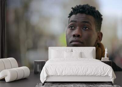 Thoughtful black man standing outside close-up face portrait in city tracking shot during winter Wall mural