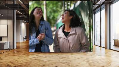 Two happy female friends walking outside. Carefree girls walk in urban street together Wall mural