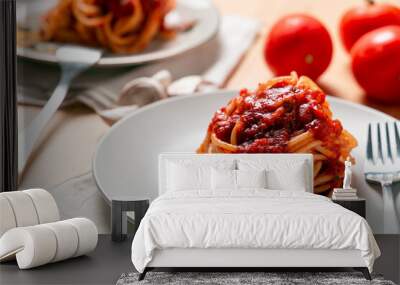 Two spaghetti nests with tomato sauce over a wooden table, with forks, kitchen towels, tomatoes and garlic Wall mural