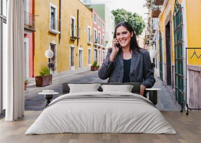 Mexican business woman talking by phone while she is walking in a Latin America city Wall mural