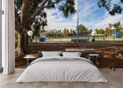 a baseball field in the park surrounded by brown benches,  lush green trees and grass at Lincoln Park with blue sky and clouds in Los Angeles California USA Wall mural