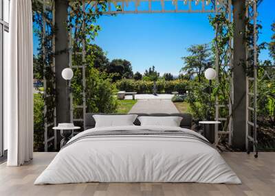 a white wooden awning in the garden covered with lush green plants and colorful flowers with a walk way leading to white flowers in the garden with blue sky at Huntington Library and Botanical Garden Wall mural