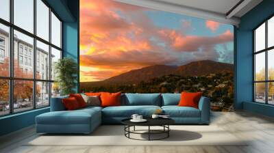 aerial shot of majestic mountains with powerful clouds and blue sky with homes, apartments and lush green trees at sunset in Monrovia California USA Wall mural