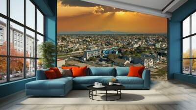 an aerial shot of the vast miles of homes and lush green trees in the city skyline with cars driving on the street, majestic mountains and powerful clouds at sunset in Huntington Beach California USA Wall mural