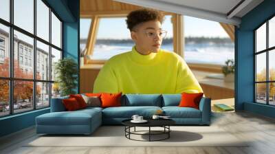 Mulatto woman with glasses and curly hair in casual attire sweater in bright neon yellow in wooden houseboat Wall mural