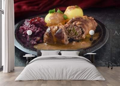 beef roulades, traditional german meal, filled meat rolls with red cabbage, potatoes and sauce on a dark plate and slate stone Wall mural