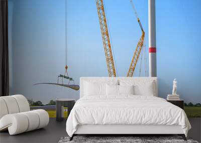 Giant crane lifting a wind turbine blade to install it onto the tower, heavy industry construction site, concept for electricity, renewable energy and power, blue sky, copy space Wall mural