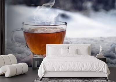 steaming hot tea in a glass cup is standing outside on a cold winter day with snow, copy space Wall mural