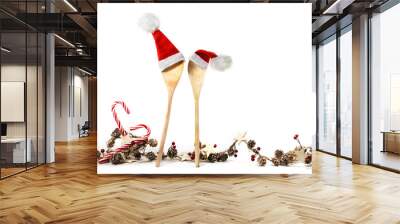 Two wooden cooking spoons with red Santa Claus hats and a Christmas decoration garland, with candy canes, cones, stars and artificial berries, isolated on a white background, copy space Wall mural