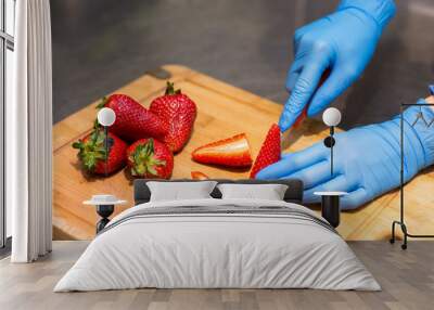 hands in blue gloves cut red strawberries on a wooden Board for fruit salad. Wall mural