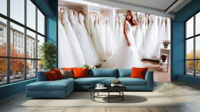 Back view of a young woman in wedding dress looking at bridal gowns on display in boutique Wall mural