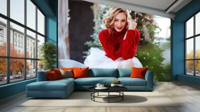 holidays, celebration and people concept - smiling woman in red sweater over christmas tree background Wall mural