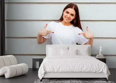 young attractive girl wearing a white t-shirt standing on a grey wall background Wall mural