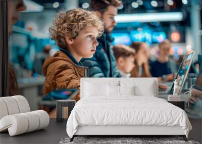 Young boy with curly hair is focused on using a laptop in modern electronics store, surrounded by other people. Wall mural