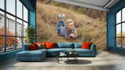 Stylish woman with short haircut hairstyle lying on grass in nature outdoors on sunset near green hills Wall mural