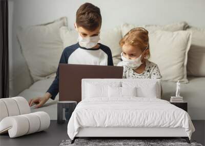 2 children, a boy and a girl are sitting in masks on the couch and playing gadgets, quarantine homew Wall mural