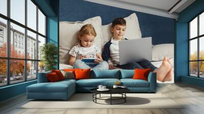 2 children, a boy and a girl sitting at home and playing games, addicted to gadgets, quarantine homework Wall mural