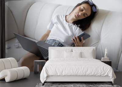 A tired woman lying on the couch near a pile of papers and a laptop, the concept of procrastination and multitasking Wall mural