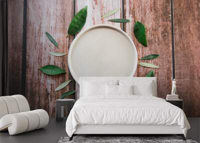 an empty beige ceramic plate surrounded by green leaves on a wooden background Wall mural