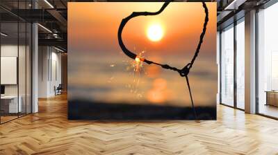 Heart-shaped sparkler burning against background of sea and rising sun at dawn. Bengal fire in shape of heart sparkling at sunrise dawn and sunset on sea. Love infatuation Valentine's Day Wall mural