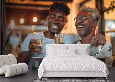 An older man and a younger adult male sharing a joyful toast with wine glasses, embodying a warm family moment at dusk. Wall mural