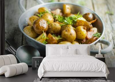 Baby young potatoes, bacon, parsley on a frying pan on a wooden background, close-up Wall mural