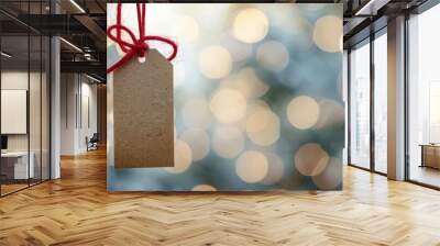 Blank gift tags dangle from red string, illuminated by a softly blurred, warm holiday background Wall mural