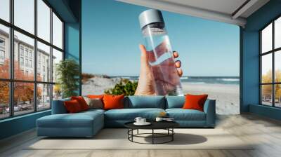 Female hand holding drinking water bottle outdoor on sea shore. Health care concept for water balance.  recyclable water container. H2O Wall mural