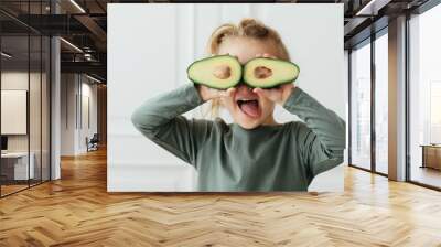 Green nature colores. Excited child girl covering eyes avocado halves white background. Healthy food and vegetarianism. vitamins,mineral,healthy Wall mural