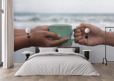 Hands of two people holding a cup of coffee or tea on beach background. Take and give or giving and receive concepts. Kindness concept. Wall mural