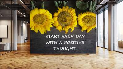 Inspirational motivational quote - Start each day with a positive thought. With yellow sun flowers on rustic wooden table background. Words of wisdom concept. Wall mural