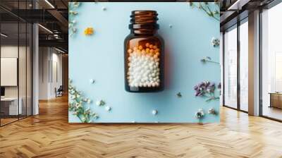 Amber glass bottle filled with homeopathic pills surrounded by delicate wildflowers on a soft blue background, showcasing natural medicine concept. Wall mural